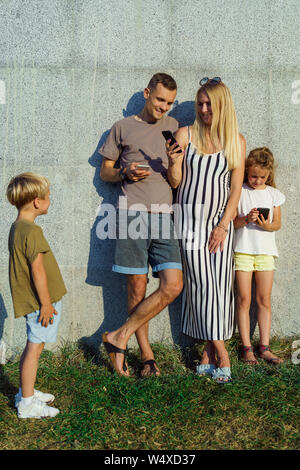 Immagine dell uomo donna e figlia con i telefoni nelle loro mani e figlio in piedi accanto al muro di cemento sulla strada Foto Stock