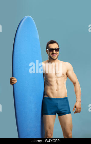 Giovane ragazzo muscolare tenendo un surf board isolato su sfondo blu Foto Stock