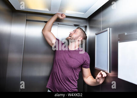 L uomo che soffre di claustrofobia intrappolato all'interno di ascensore urlando Foto Stock