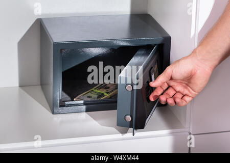 Una mano d'uomo mettendo Bundle di banconota in una cassetta di sicurezza Foto Stock