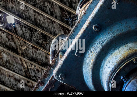 Peeling blu vernice su ferro forgiato macchinari sotto il soffitto di legno aperto al cielo attraverso le assicelle mancanti. Immagine presa in magazzino abbandonato. Foto Stock