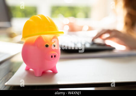 Close-up di Rosa Piggybank con Casco giallo sulla scrivania in ufficio Foto Stock