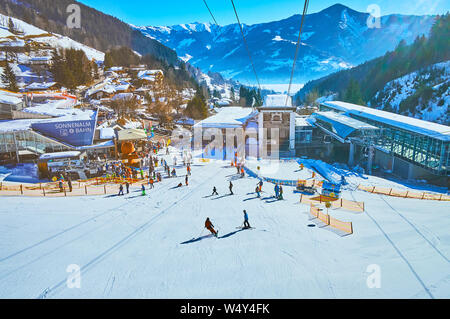 ZELL AM SEE, Austria - 28 febbraio 2019: emozionante viaggio sulla moderna funivia con una vista sulla sua stazione inferiore, sciatori sul monte Shcmitten piste Zel Foto Stock