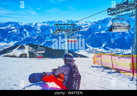 ZELL AM SEE, Austria - 28 febbraio 2019: l'inverno il paesaggio alpino con riding skilift, dolce pendio del monte Schmitten e stanco snowboarder, sittin Foto Stock