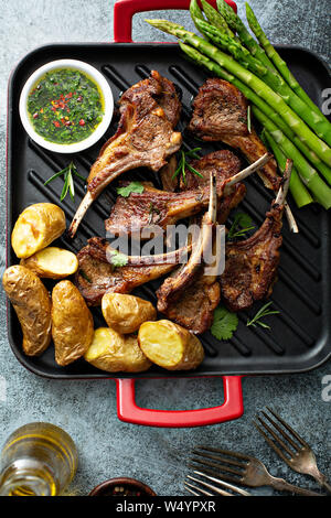 Costolette di agnello grigliate con salsa alle erbe verdi, asparagi e patate Foto Stock