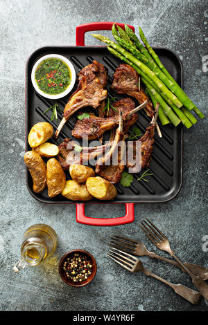 Costolette di agnello grigliate con salsa alle erbe verdi, asparagi e patate Foto Stock