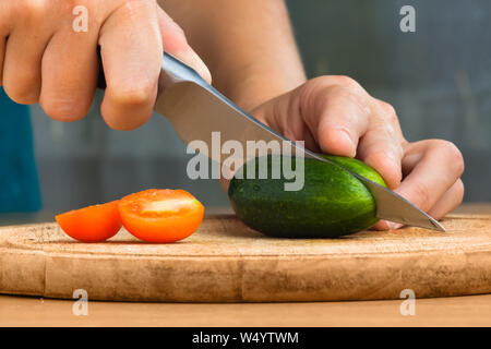 Le mani della donna per Affettare cetrioli e pomodori sul tagliere per insalata, primo piano Foto Stock