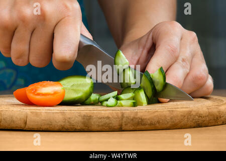 Le mani della donna tritare il cetriolo sul tagliere per insalata, primo piano Foto Stock