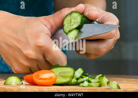 Le mani della donna tritare il cetriolo sul tagliere per insalata, primo piano Foto Stock