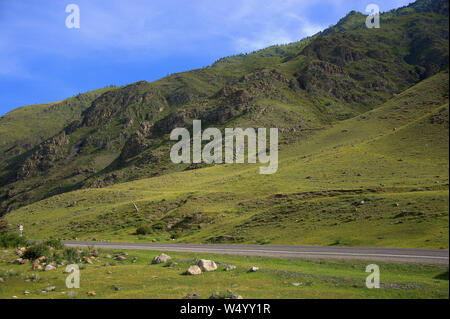 Strada asfaltata attraversando una valle verde racchiuso tra le montagne. Altai, Siberia, Russia. Foto Stock