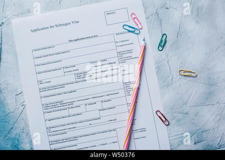 Il riempimento della Schengen Visa Application Form da sopra. Multicolore di fermagli per carta e penna. Foto Stock