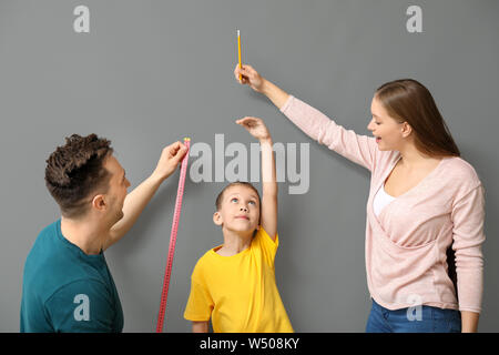 I genitori Misurazione altezza del loro figlio vicino al muro grigio Foto Stock