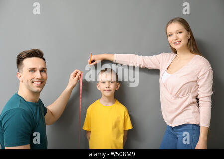 I genitori Misurazione altezza del loro figlio vicino al muro grigio Foto Stock