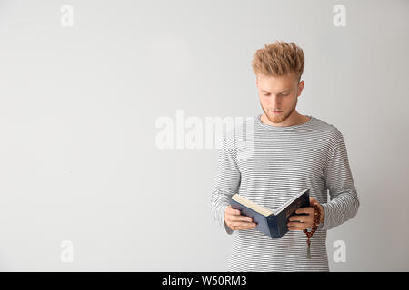 I religiosi giovane uomo leggendo la Bibbia su sfondo chiaro Foto Stock