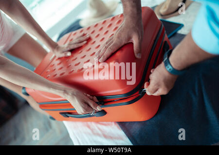 Ottenere pronto. Le mani di due persone spingere su un lato di una valigia cercando di chiuderlo e zip. Foto Stock