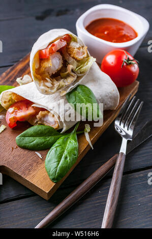 Close-Up tortilla avvolge con gamberi fritti, lattuga e pomodoro su un tagliere di legno. Cibo sano. Colpo verticale Foto Stock