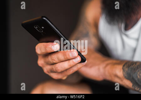 Uomo con la barba e i tatuaggi tenendo in mano nero smartphone close up Foto Stock