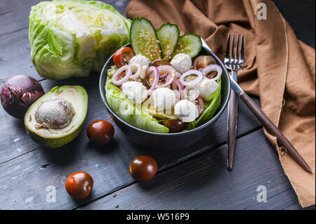 Insalata di verdure con insalata di ghiaccio, il cetriolo, la cipolla, i pomodori ciliegia, mozzarella e olio di sesamo. Cibo sano. In primo piano Foto Stock