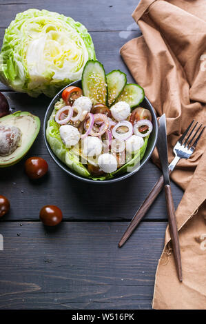 Insalata di verdure con insalata di ghiaccio, il cetriolo, la cipolla, i pomodori ciliegia, mozzarella e olio di sesamo. Cibo sano. Colpo verticale Foto Stock