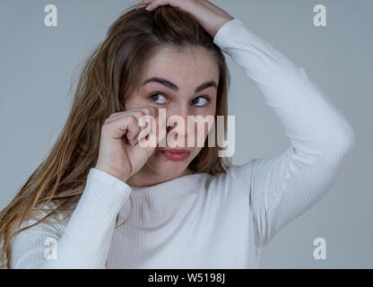 Ritratto di bella ragazza adolescente divertente con la faccia triste guardando dolce e carino. Femmina millenario rendendo silly infelice gesti isolati su folle b Foto Stock