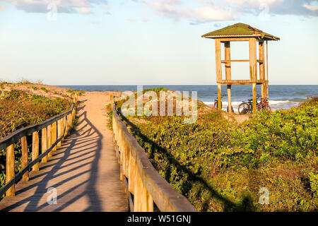 Bagnino capanna sulla spiaggia Navegantes nel tardo pomeriggio con la passerella di legno sulle dune e vegetazione nativa, cielo blu con nuvole Foto Stock