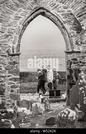 Gruppo di famiglia passando per arcata in pietra di Abbazia in rovina in Ballinskelligs, nella contea di Kerry, Irlanda Foto Stock