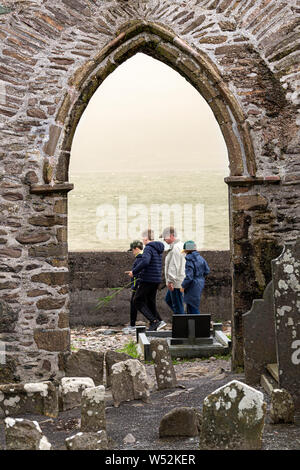 Gruppo di famiglia passando per arcata in pietra di Abbazia in rovina in Ballinskelligs, nella contea di Kerry, Irlanda Foto Stock