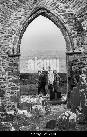 Gruppo di famiglia passando per arcata in pietra di Abbazia in rovina in Ballinskelligs, nella contea di Kerry, Irlanda Foto Stock