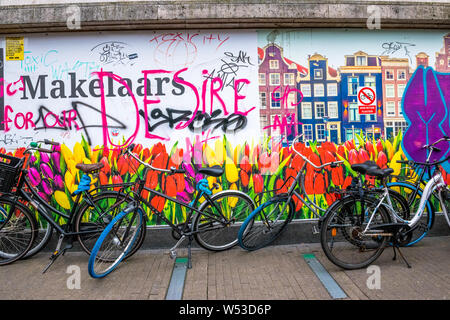 Biciclette olandesi nella parte anteriore di un grande poster del Dutch Canal alloggiamento e tulipani e con graffiti. Foto Stock