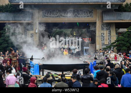 Lavoratori cinesi in costumi tradizionali a fare dieci-ton Laba Congee, o otto tesori porridge, per i visitatori in un gigante di pentola in ferro con un diamete Foto Stock