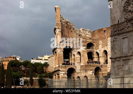 La parte esterna del Colosseo nella luce della sera con i turisti la visualizzazione delle rovine. Il cielo dietro è scuro, grigio e tempestoso. Foto Stock