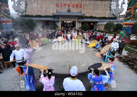 Lavoratori cinesi in costumi tradizionali a fare dieci-ton Laba Congee, o otto tesori porridge, per i visitatori in un gigante di pentola in ferro con un diamete Foto Stock