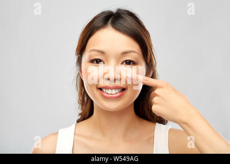 Sorridenti giovane donna asiatica di toccare il suo volto Foto Stock