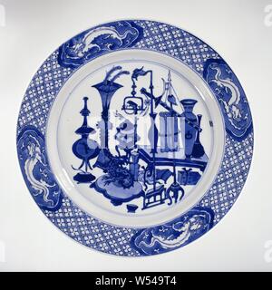 Piastra con antichità e draghi, piastra di porcellana con la parete verticale e il bordo smussato, dipinta in underglaze blu. Sul ripiano antiquariato (vasi, penne di pavone, libri, cartigli incensiere) e splendidi oggetti come una immagine di un drago su un cuscino e un pappagallo su un cavalletto, al confine con il tovagliolo lavori intervallati con cartouches lobata con un drago in bianco salvato in uno sfondo blu, sul lato inverso gli oggetti di valore (Diamond, perla, pietra musicale), Lucky simboli (shell) e un attributo del Otto Immortali (nacchere). Contrassegnato sul fondo di un ramo di fiori in un doppio cerchio Foto Stock