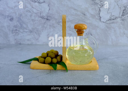 Set di olio di oliva e di foglie su sfondo marmo, bottiglia di vetro con olio d'oliva sulla tabella di cemento, bottiglia di vetro del premio di olio vergine di oliva Foto Stock