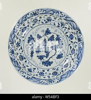 Piatto piatto con vitigni e cartigli floreali, piatto porcellana dipinta in underglaze blu. Sul ripiano di un vitigno. La parete con un flusso continuo di fiori e il bordo con una band con onde di vorticazione. La parete di fondo con un fiore della vigna. Porcellana Ming in blu e bianco., anonimo, Cina, c. 1400 - c. 1424, Ming-dinastia (1368-1644) / Jianwen-periodo (1399-1402) / Yongle-periodo (1403-1424), porcellana (materiale), smalto, cobalto (minerali), di vetrificazione, h 7.5 cm d 38 cm d 24,5 cm Foto Stock
