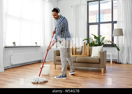 Uomo in cuffie con mop piano di pulizia a casa Foto Stock