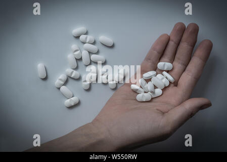 Mano che tiene molti white la prescrizione di farmaci, medicina compresse o pillole di vitamine in una pila - Concetto di sanità, dipendenza da oppioidi, medicamento abuso Foto Stock