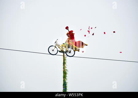 Un acrobatico cinese attore vestito come il dio della ricchezza scende hongbao (buste rosse con lucky money) verso il basso per il pubblico come lui corre in una bicicletta su Foto Stock