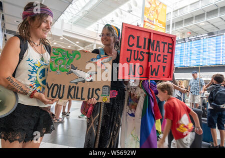 26 luglio 2019, il Land della Baviera, Monaco di Baviera: due donne prendono parte ad una azione di protesta all'aeroporto di Monaco di Baviera all'inizio dell'estate vacanze in Baviera con manifesti con le scritte "ci uccidete' e 'giustizia climatica ora! Circa 40 persone hanno protestato contro i battenti qui. Foto: Peter Kneffel/dpa Foto Stock