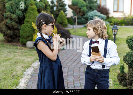 Carino ragazzo biondo e carina ragazza, anno scolastico tempo di divertimento all'aperto. I bambini mangiare cioccolato. Foto Stock