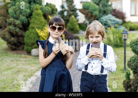 Carino ragazzo biondo e carina ragazza, anno scolastico tempo di divertimento all'aperto. I bambini mangiare cioccolato. Foto Stock