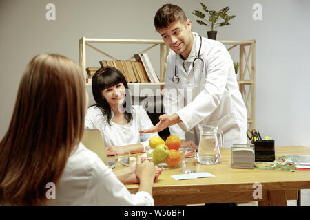 Sorridente nutrizionisti che mostra una dieta sana piano per paziente. Giovane donna la visita di un medico per avere una nutrizione raccomandazioni. Concetto di stile di vita sano e cibo, medicina e trattamento. Foto Stock