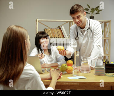 Sorridente nutrizionisti che mostra una dieta sana piano per paziente. Giovane donna la visita di un medico per avere una nutrizione raccomandazioni. Concetto di stile di vita sano e cibo, medicina e trattamento. Foto Stock