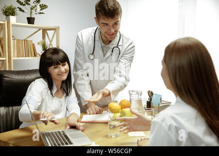 Sorridente nutrizionisti che mostra una dieta sana piano per paziente. Giovane donna la visita di un medico per avere una nutrizione raccomandazioni. Concetto di stile di vita sano e cibo, medicina e trattamento. Foto Stock