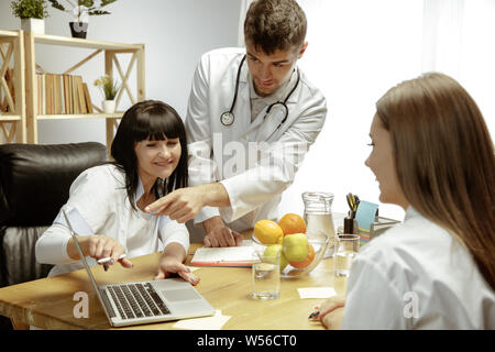 Sorridente nutrizionisti che mostra una dieta sana piano per paziente. Giovane donna la visita di un medico per avere una nutrizione raccomandazioni. Concetto di stile di vita sano e cibo, medicina e trattamento. Foto Stock