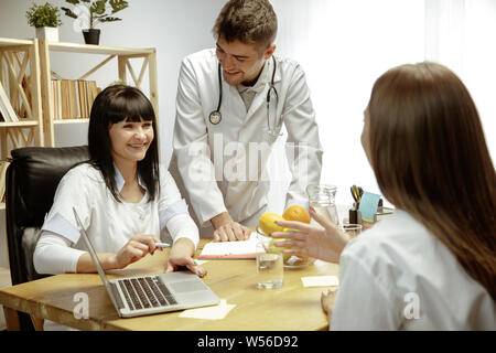 Sorridente nutrizionisti che mostra una dieta sana piano per paziente. Giovane donna la visita di un medico per avere una nutrizione raccomandazioni. Concetto di stile di vita sano e cibo, medicina e trattamento. Foto Stock