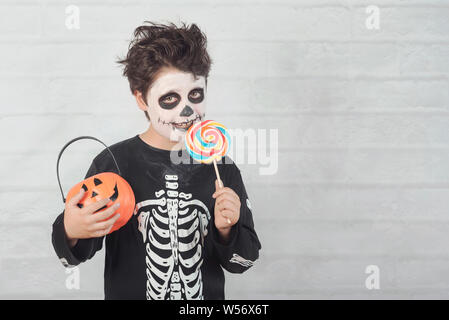 Happy Halloween.divertente bambino in un costume di scheletro di mangiare lecca-lecca di halloween contro Sfondo mattone Foto Stock