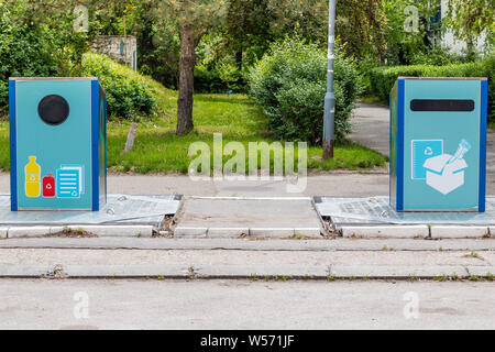 Due blue cestini con simbolo di riciclaggio per i vari tipi di rifiuti di plastica, lattine e carta, sul marciapiede. Foto Stock