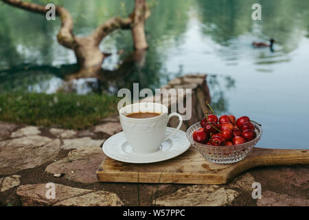 Tazza di caffè e le ciliegie sul tagliere in natura Foto Stock